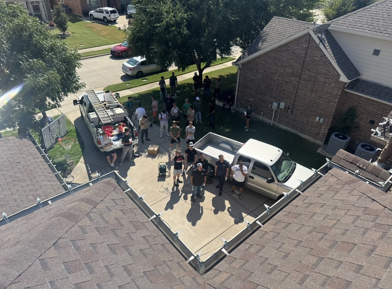 Drone shot of installer training day — crew on ground, clips on roofline, trucks in driveway